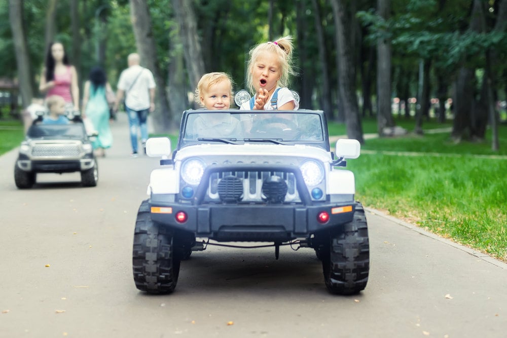 Two children riding an electric ride on jeep convertible on a path