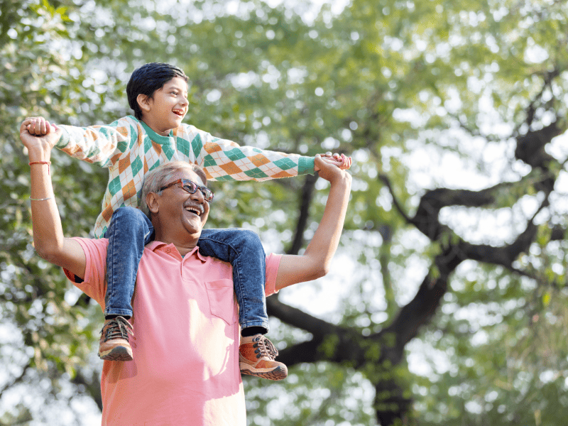 A child sits on their grandad’s shoulders as they play outside