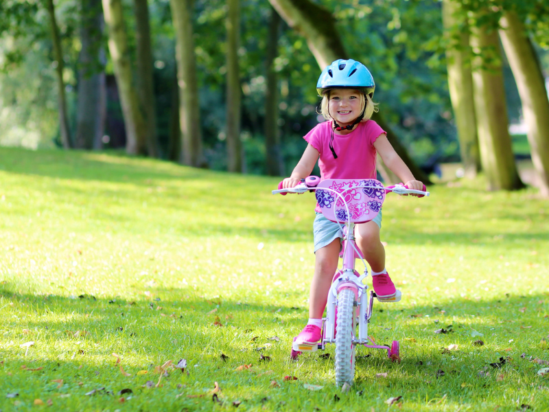 A happy girl rides her bike across a lawn towards the camera