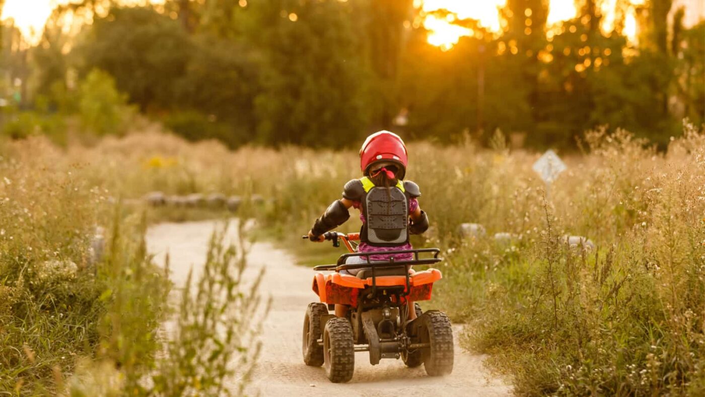 a child riding a quad bike on a dirt track, heading towards the sunset